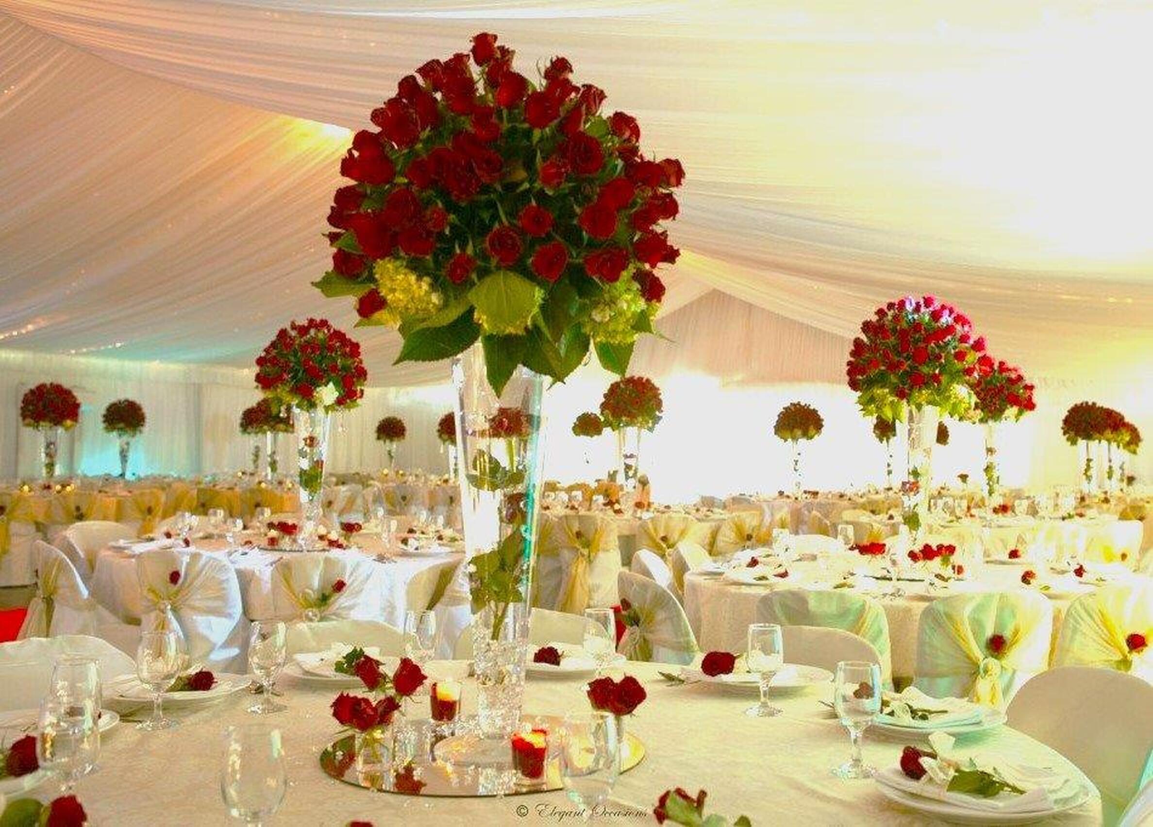 Reception tables styled with tall red floral centrepieces and warm lighting